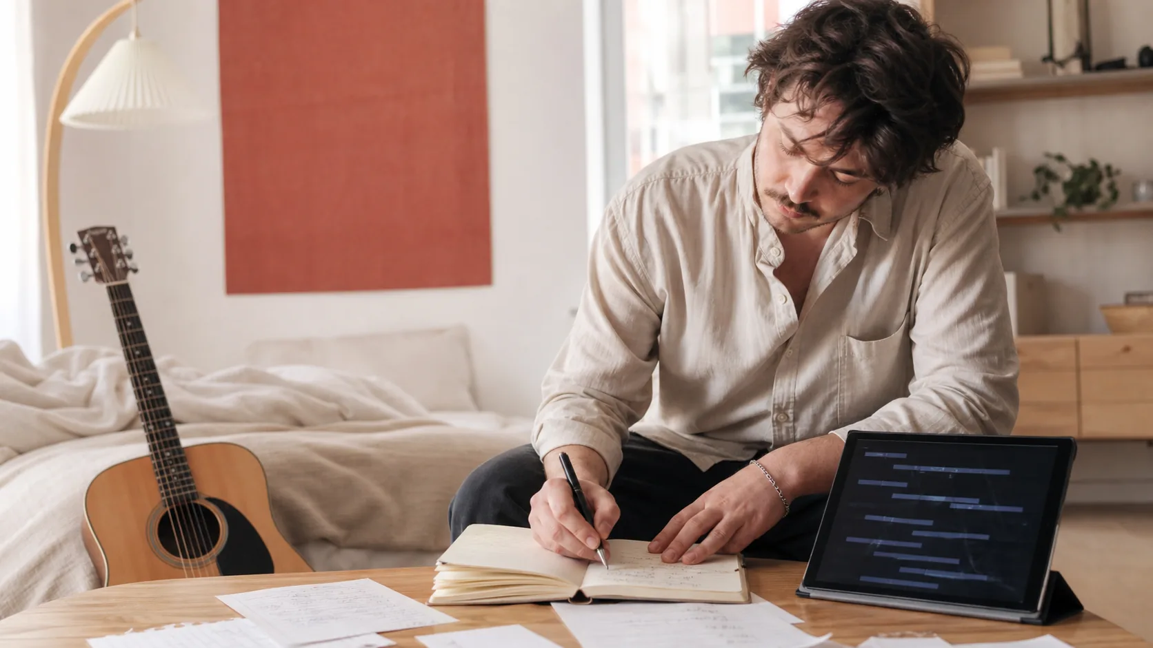 Songwriter turning rough ideas into lyrics with acoustic guitar nearby